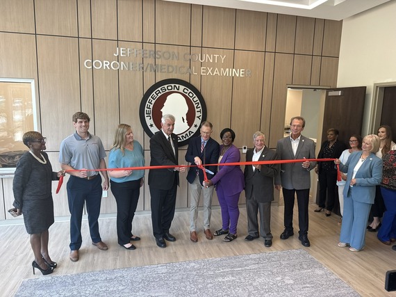 County Commissioners cutting the ribbon on the new Coroner's office. Standing in front of the County Seal on the wall