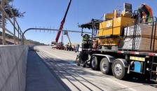 Crews prepare equipment for final striping of the pavement, while a crane operator lifts an overhead sign into place. 