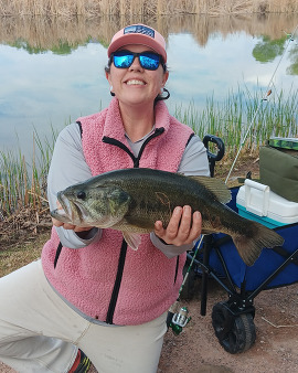 woman holding bass in front of forest stream