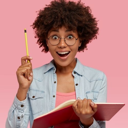 Young Black woman with glasses, in a denim jacket, looking like she had an idea on a pink background