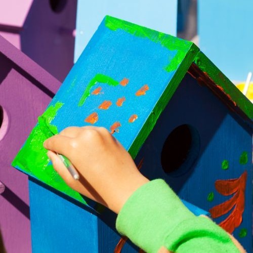 Child hand painting a birdhouse bright colors of blue and purple.