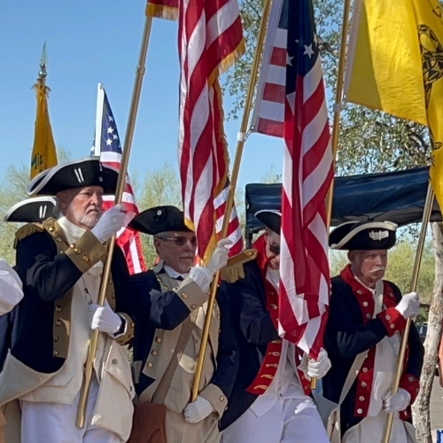 A group of people in colonial-era attire holding American flags and other banners.