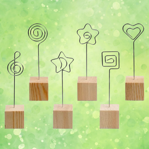 The background is soft green watercolor with a bokeh effect. In the foreground are photo holders made of wire and wood blocks. 
