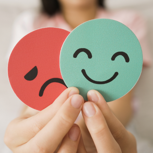A person holds up two round cutouts, one red with a sad face and one teal with a happy face