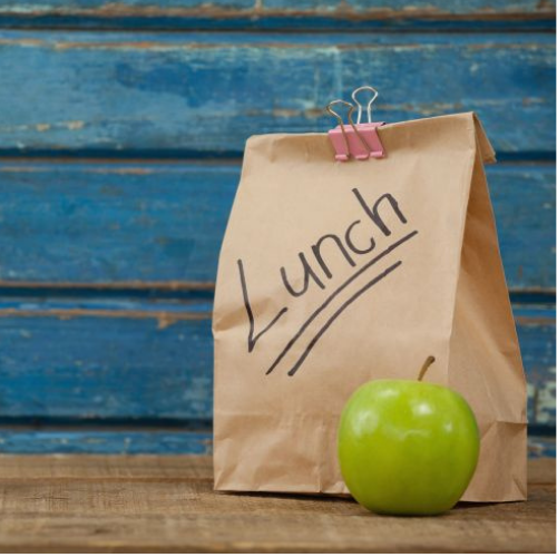 A brown paper lunch bag with the word "Lunch" written on it in black marker, clipped shut with pink binder clips.
