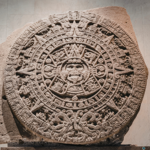 The Aztec Sun Stone, a large carved stone disc featuring intricate glyphs and a central face, is displayed upright.