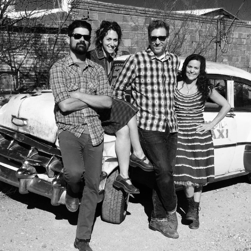 A black and white photo of four people posing in front of a vintage taxi.
