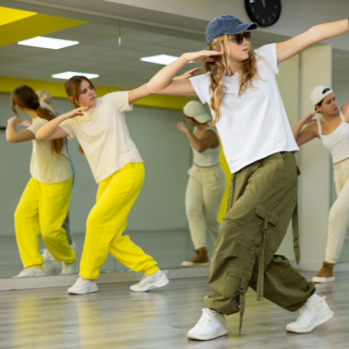 A group of people in athletic wear dancing in a studio with mirrors reflecting their movements.