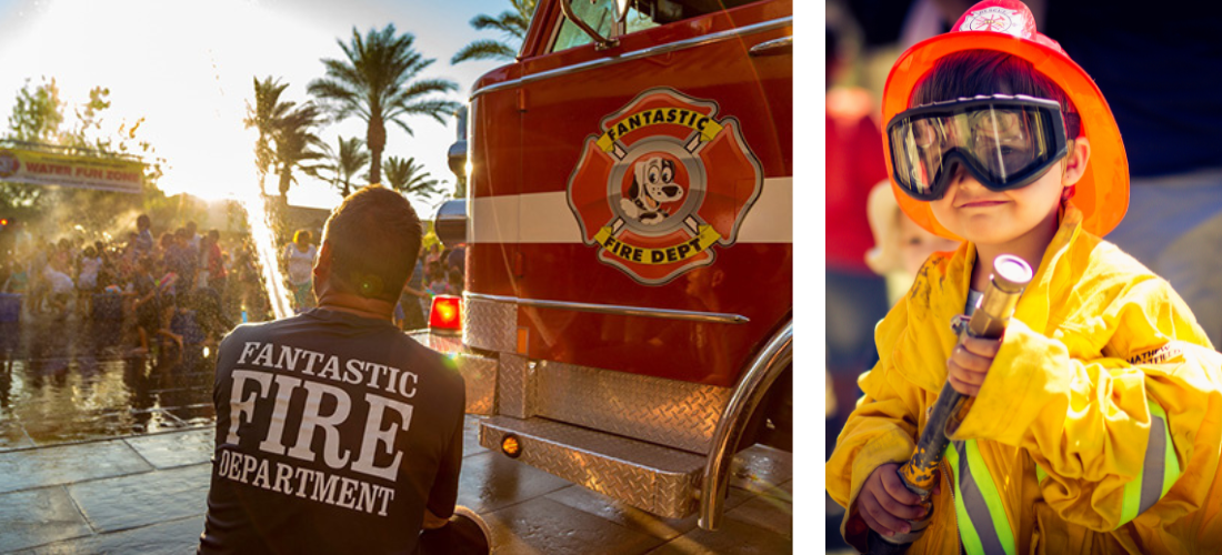 A firefighter wearing a shirt that says "Fantastic Fire Department" crouches next to a fire truck as a group of people enjoy a water spray 