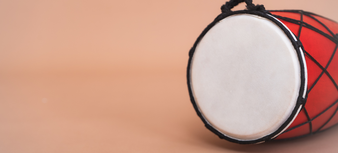 A close-up of a red dholak drum with a white head, on a plain background.