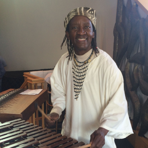 A musician wearing a patterned hat and traditional clothing plays a marimba with mallets.