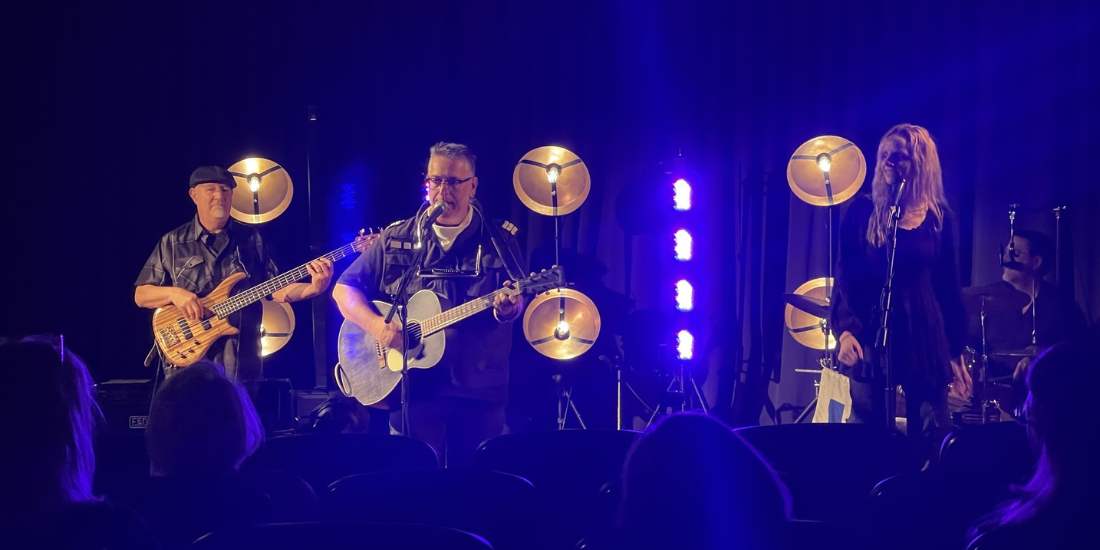 A band performs on stage with blue lighting and large circular lights behind them. 
