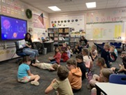 Councilmember reading book to group of elementary students sitting on floor in classroom