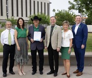 Council and Mayor wearing green, standing, smiling, holding proclamation 