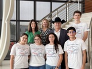 Councilmember and Mayor standing with students in Sister Cities t shirts on staircase at City hall