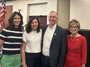 Councilmembers and two other people smiling and looking at camera in ballroom