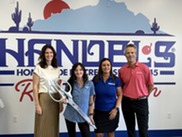 4 people standing in front of Handel's sign, one holding giant scissors