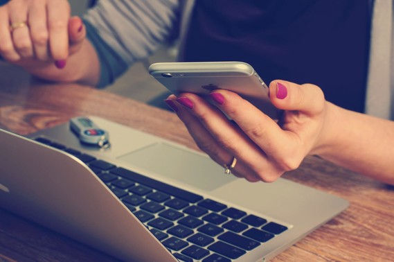 Person holding a cell phone while working on a laptop