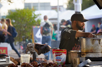 A person stirring a large pot in an outdoor cooking setting
