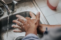 Soapy hands being washed over a sink with running water