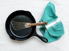 a cast iron pan with a cooking utensil and dish towel