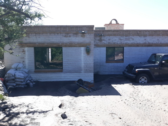 image of a house after flooding. mud is covering part of jeep tire and there is an overturned wheelbarrow. thick mud and sediment covers the ground