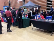members of the public stand in line at a job booth 