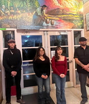 students and teacher pose in front of mural