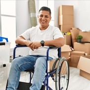 Image: Young man in a wheelchair smiling, surrounded by moving boxes