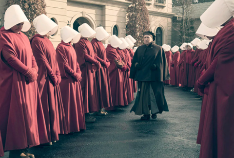 Frame of movie Handmaids Tale of woman in red covered dress with face coverings, looking down