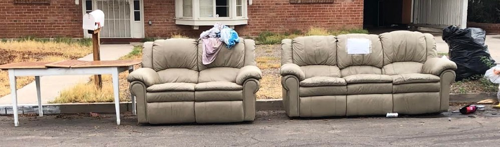 Picture showing some sofas, table, and trash in the street