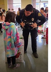TPD uniformed officer bends down to listen to child in a slightly oversized, warm coat at a holiday event.