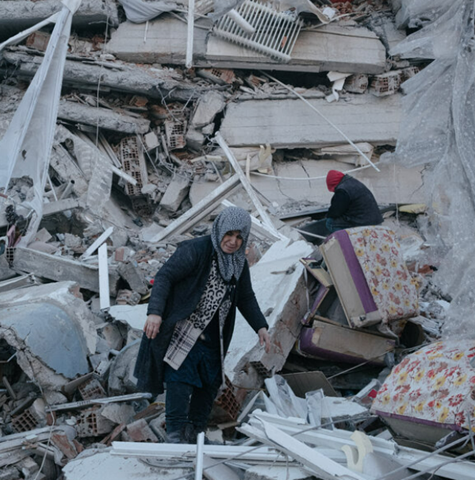 Picture of the aftermath of the Turkey earthquake showing older lady walking on the rubble