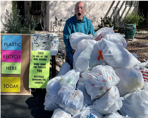 Picture of a gentleman stands in front of pile of plastic bags during plastic collection event