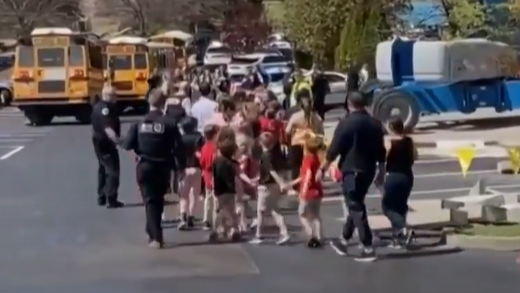 Picture shows kids walking to the school buses with the police officers and teachers