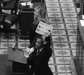 Picture shows one of the Tennessee legislators leads the protest with a megaphone while holding up "protect kids no guns" sign