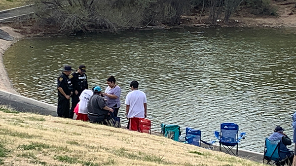 Young people fishing at a small lake with TPD members in uniform standing by
