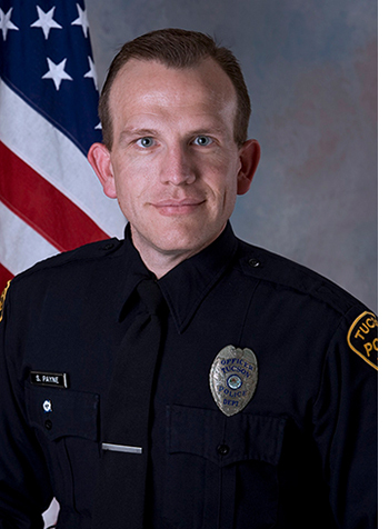 TPD Officer Sean Payne, in uniform, in front of an American flag