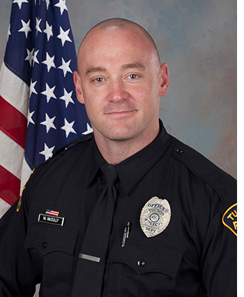 Ofc McCully in uniform in front of an American flag