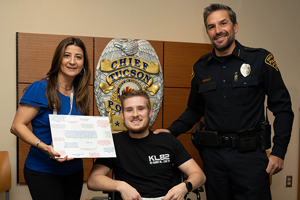 TPD Officer Kyle Lorenz is seated between Nohemy Hite and Tucson Police Chief Chad Kasmar, who are standing