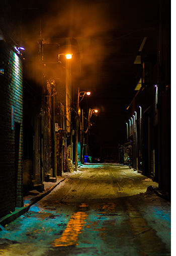 Dark alley with minimal streetlights reflected in a few puddles