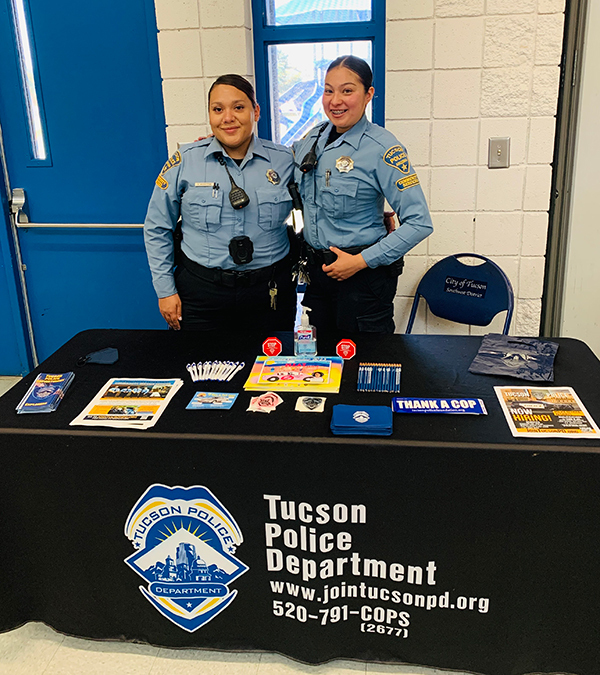 Two TPD Community Service Officers stand behind a table for TPD recruiting at a resource fair