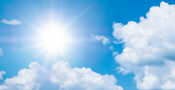 Summer sun shining in the sky surrounded by fluffy clouds