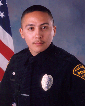 Department photo of a TPD officer in uniform in front of an American flag.