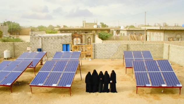 Picture shows women with black burqa stands next to the microgrid power in Yemen