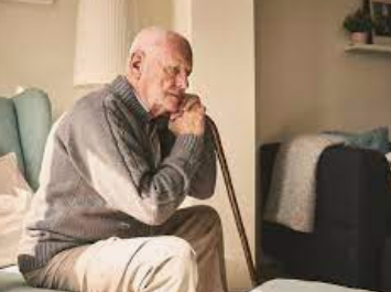 An elderly gentleman in a grey top sit on the couch 