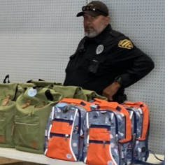 Uniformed ODW TPD officer standing behind a table with backpacks to give away.