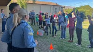 TPD ODW CSOs in uniform stand on the sidelines outside while youth play.