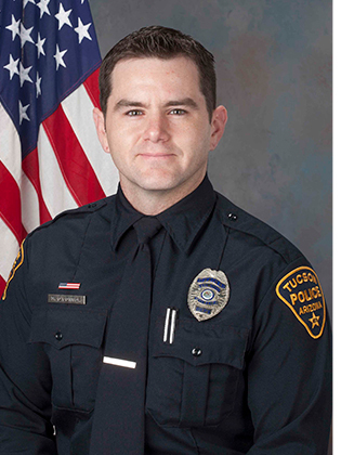 Department photo of officer in uniform in front of an American flag.