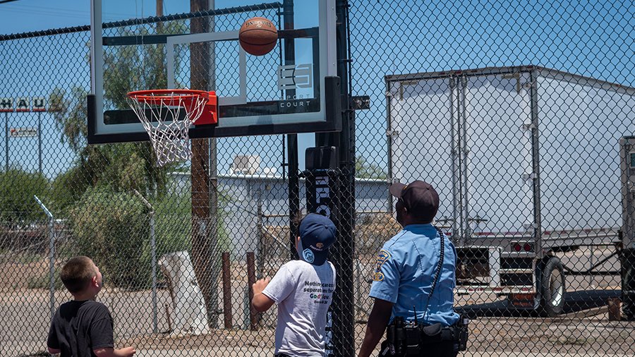 TPD ODM CSO, in uniform, playing basketball outside with two little boys, the basketball in the air just above the net.